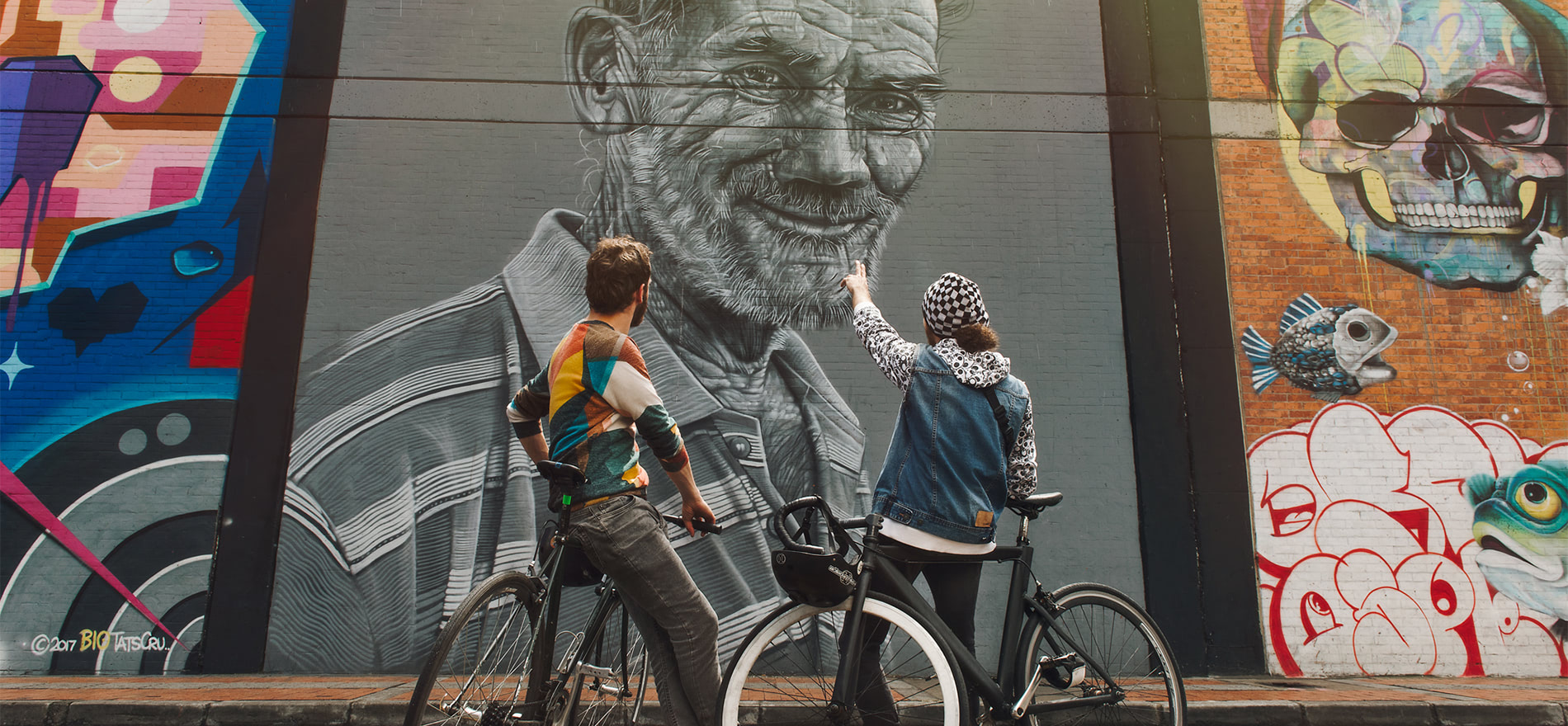 pareja en bicicleta de espaldas observando un mural del Colombia street art.