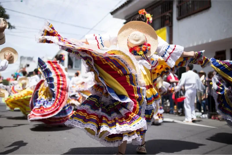 Dancer wearing a vibrant folkloric costume (yellow, red, and blue) and a traditional wide-brimmed hat, spinning in a street.