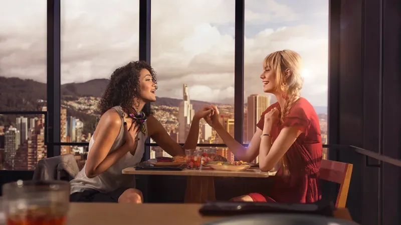 Dos chicas tomadas de la mano disfrutan de un almuerzo en un restaurante con la ciudad de fondo