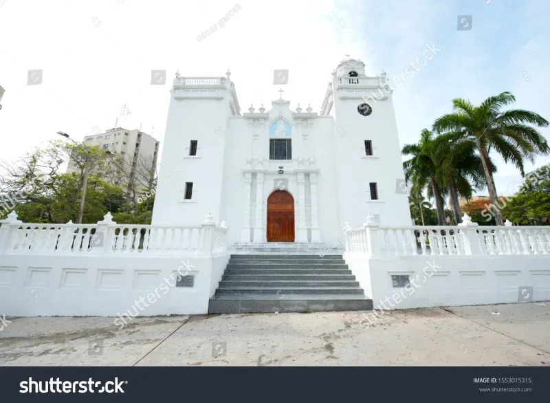 Iglesia de la Inmaculada Concepción en Barranquilla vista desde afuera, donde se impone el color blanco en su fachada rodeada de un cielo azul y algunas plantas, hace parte de las Iglesias y Capillas de Barranquilla