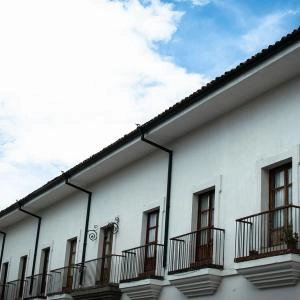 Fachada de edificio colonial blanco con balcones de hierro y cielo azul con nubes.