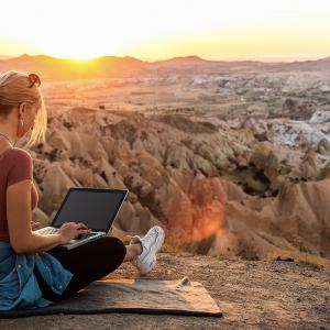 Una mujer que viaja por negocios trabaja en su computadora en medio de un paisaje desértico.