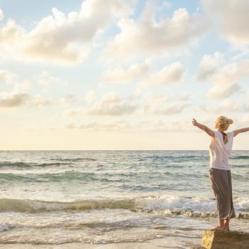 Una mujer extiende sus brazos en la playa frente al mar, disfrutando del turismo mindfulness.