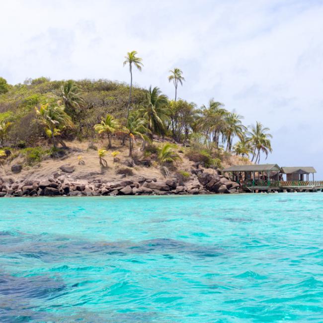 The blue sea of San Andrés with a coast full of vegetation and little wood structures.