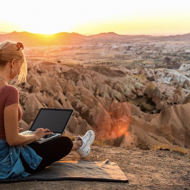 Una mujer que viaja por negocios trabaja en su computadora en medio de un paisaje desértico.